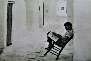 A child reads a newspaper in a narrow street of Mykonos. 1960s era photo.